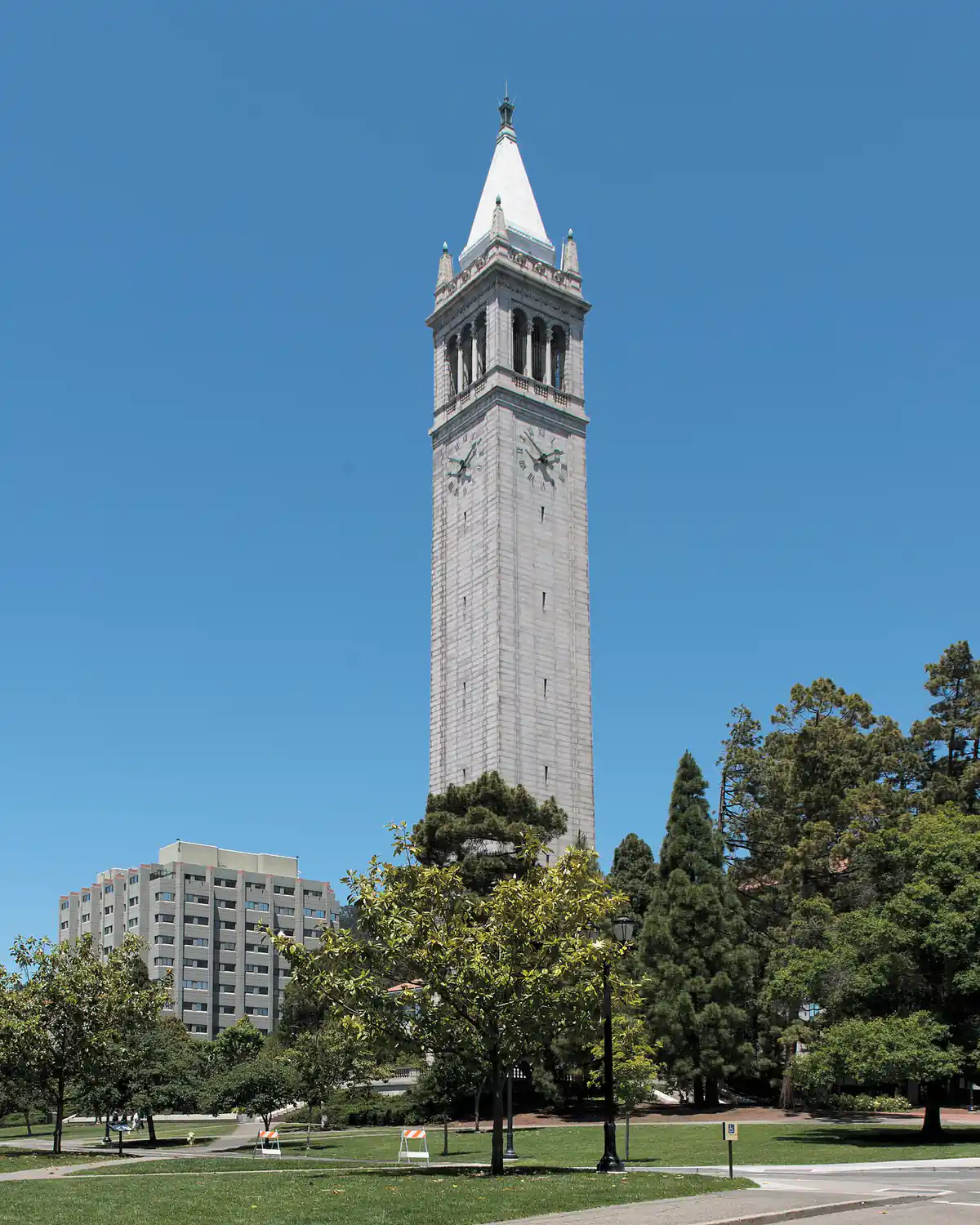UC Berkeley's Sather Tower in daylight, rising above a lawn and trees under a clear blue sky.